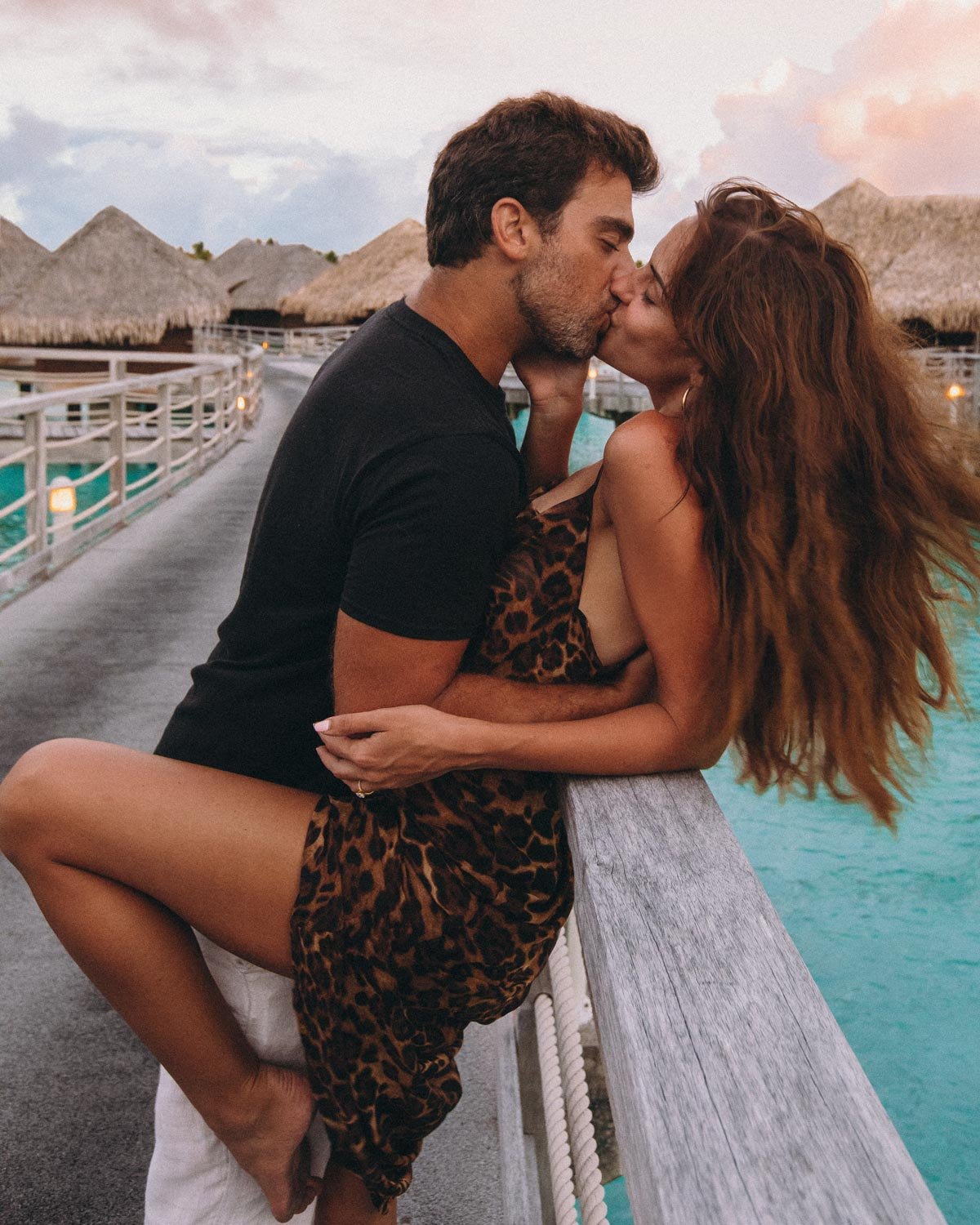 A couple sharing a kiss beside turquoise water and overwater bungalows