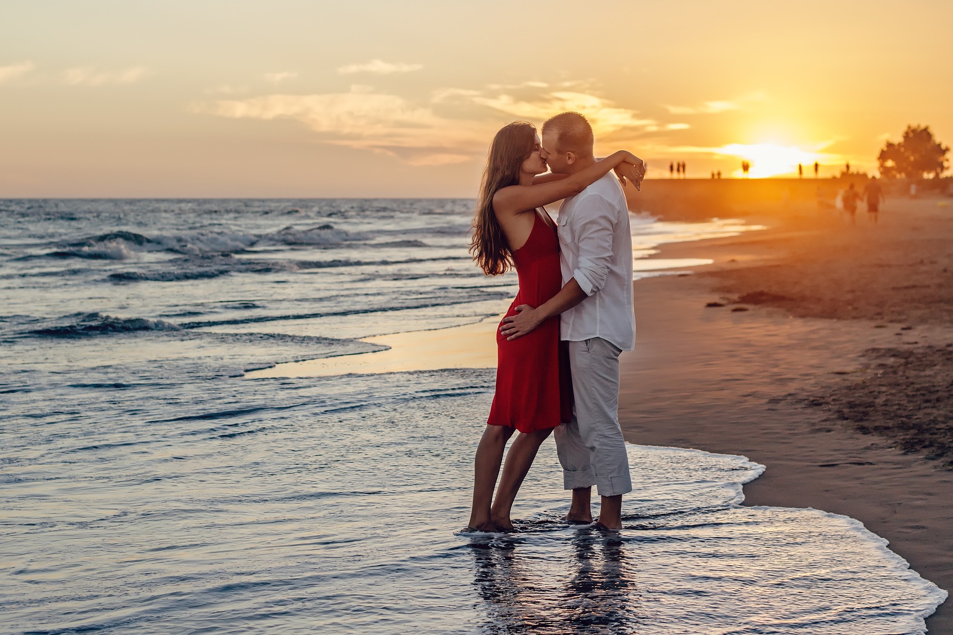 A couple embracing and kissing at the edge of the sea at sunset